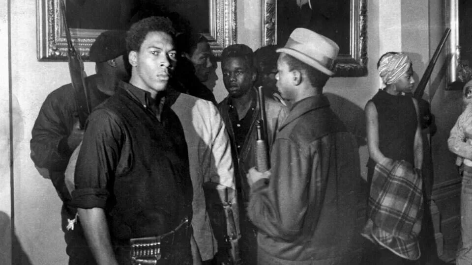 Black-and-white photograph of a group of people, several carrying long guns, inside a civic building.